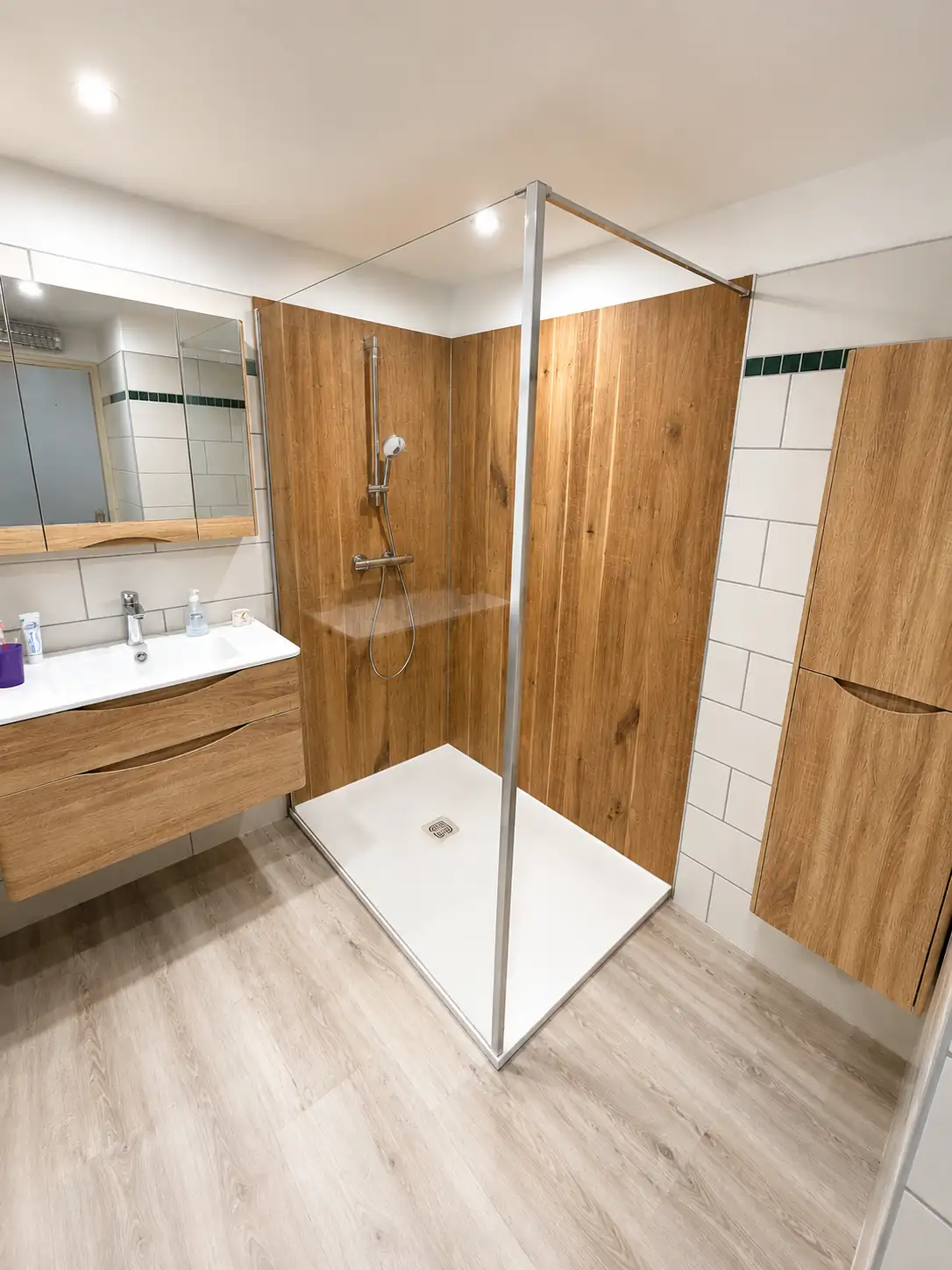 Salle de bain rénovée par Erwan Pronost : douche à l'italienne avec paroi vitrée et panneaux muraux effet chêne